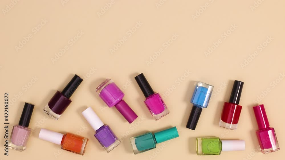 Nail polishes bottles falling on beige background. Stop motion flay lay