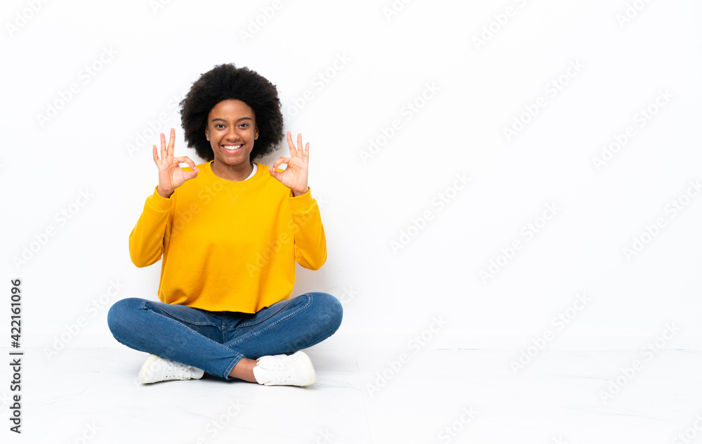 Young African American woman sitting on the floor showing an ok sign with fingers Young African American woman sitting on the floor showing an ok sign with fingers