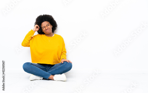 Young African American woman sitting on the floor having doubts and with confuse face expression © luismolinero