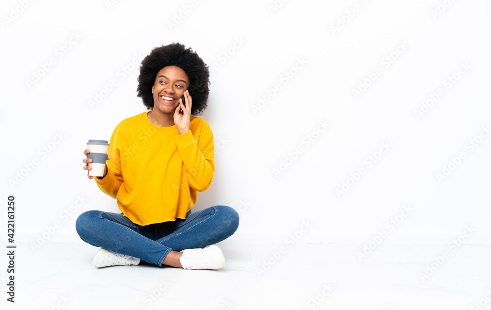 Young African American woman sitting on the floor holding coffee to take away and a mobile Young African American woman sitting on the floor holding coffee to take away and a mobile