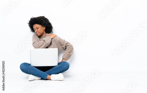 Young African American woman with a laptop sitting on the floor suffering from pain in shoulder for having made an effort © luismolinero