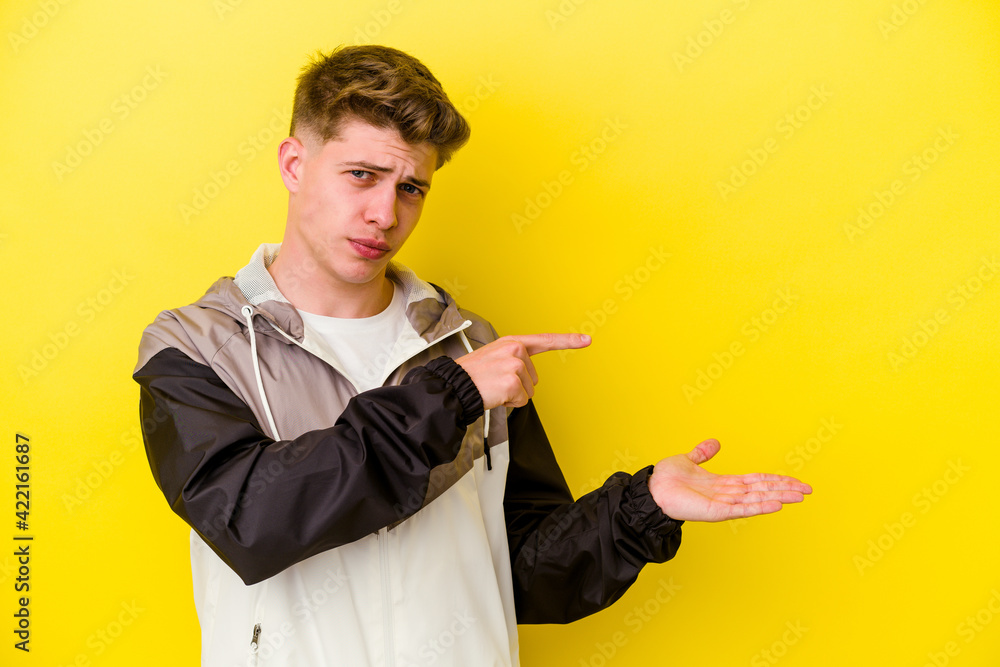 Young caucasian man isolated on yellow background excited holding a copy space on palm.