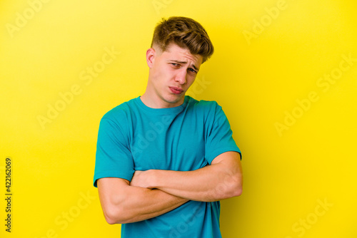 Young caucasian man isolated on yellow background blows cheeks, has tired expression. Facial expression concept.