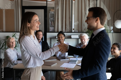 Happy Caucasian businessman shake hand of smiling female employee worker congratulate greet with job promotion. Excited diverse businesspeople colleagues handshake get acquainted at meeting.
