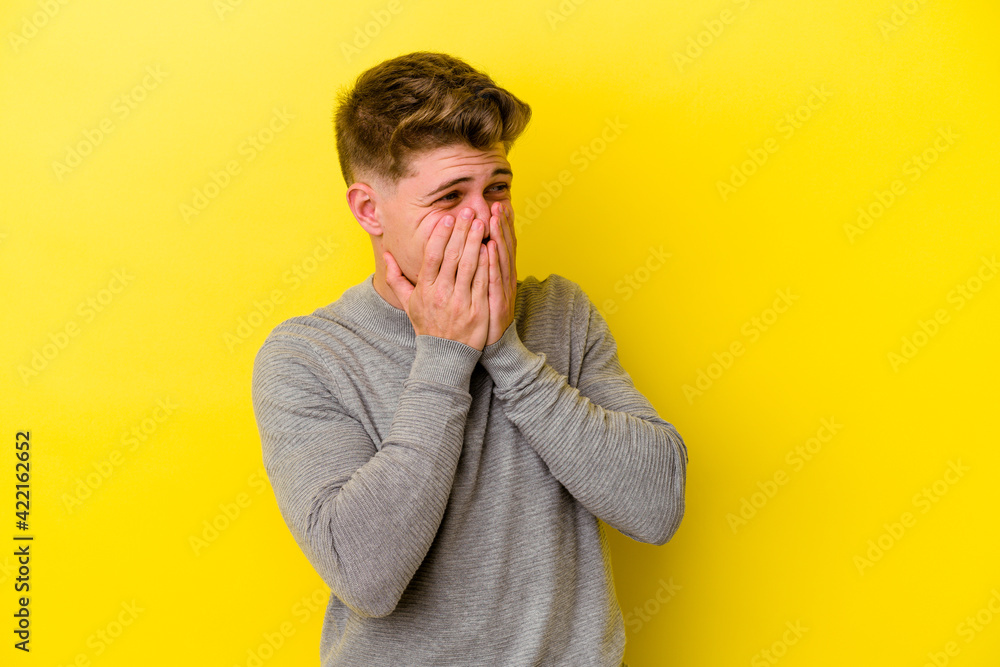 Young caucasian man isolated on yellow background laughing about something, covering mouth with hands. Young caucasian man isolated on yellow background laughing about something, covering mouth with hands.