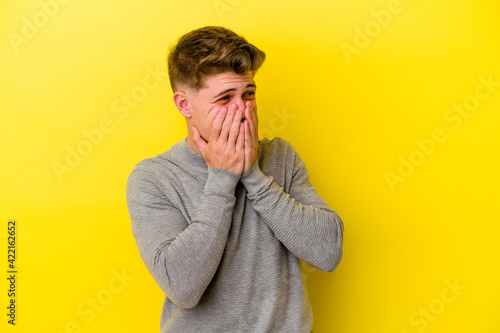 Young caucasian man isolated on yellow background laughing about something, covering mouth with hands. © Asier
