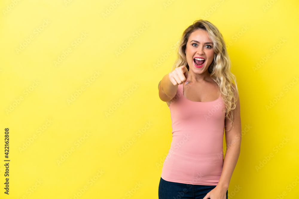 Young Brazilian woman isolated on yellow background surprised and pointing front Young Brazilian woman isolated on yellow background surprised and pointing front