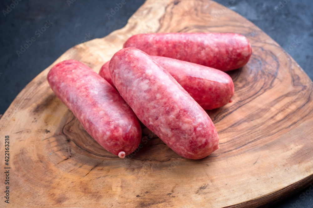 Traditional Italian raw salsiccia fresco meat sausage offered as close-up on a rustic wooden cutting board Traditional Italian raw salsiccia fresco meat sausage offered as close-up on a rustic wooden cutting board