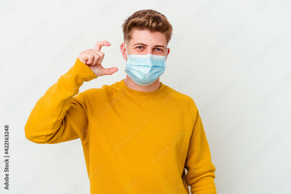 Young man wearing a mask for coronavirus isolated on white background holding something little with forefingers, smiling and confident. Young man wearing a mask for coronavirus isolated on white background holding something little with forefingers, smiling and confident.