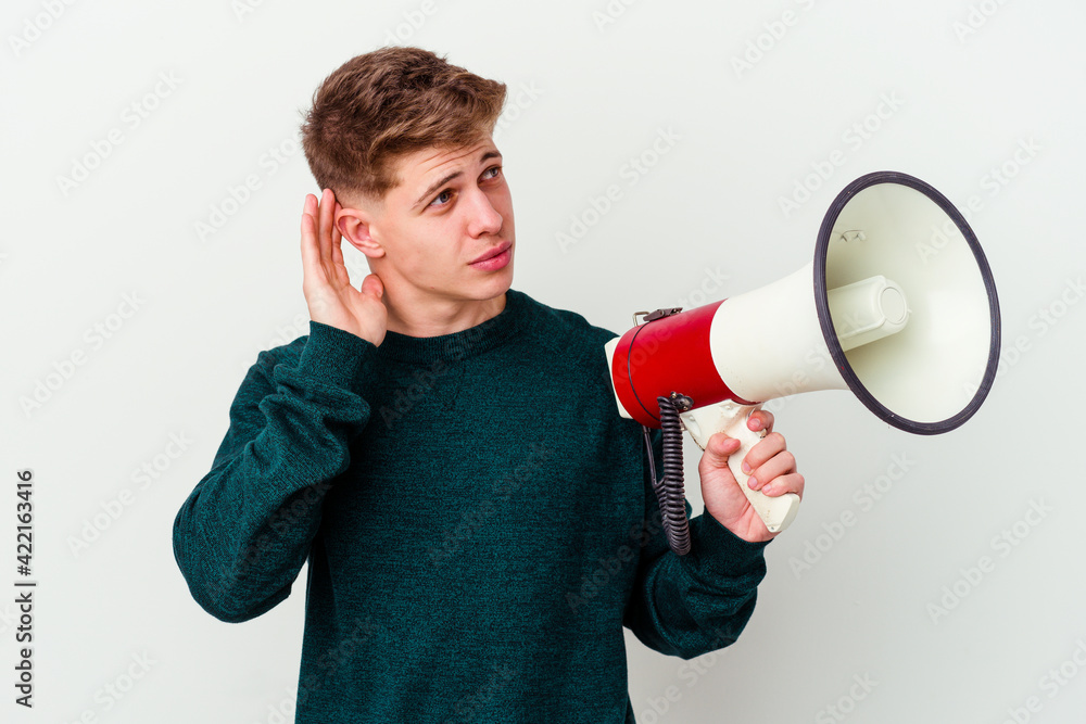 Young caucasian man holding a megaphone isolated on white background trying to listening a gossip. Young caucasian man holding a megaphone isolated on white background trying to listening a gossip.