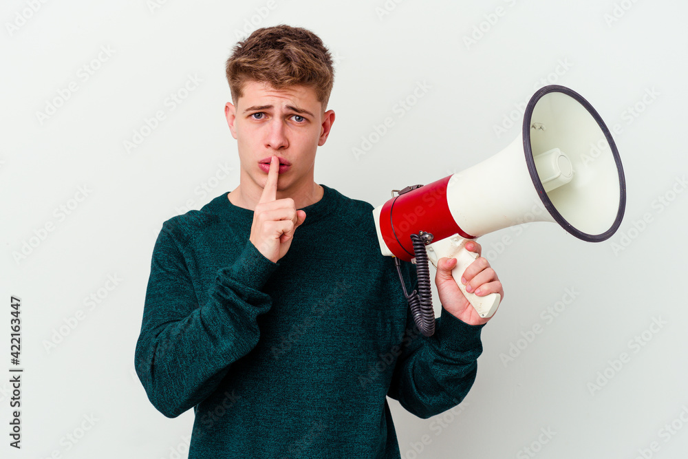 Young caucasian man holding a megaphone isolated on white background keeping a secret or asking for silence. Young caucasian man holding a megaphone isolated on white background keeping a secret or asking for silence.