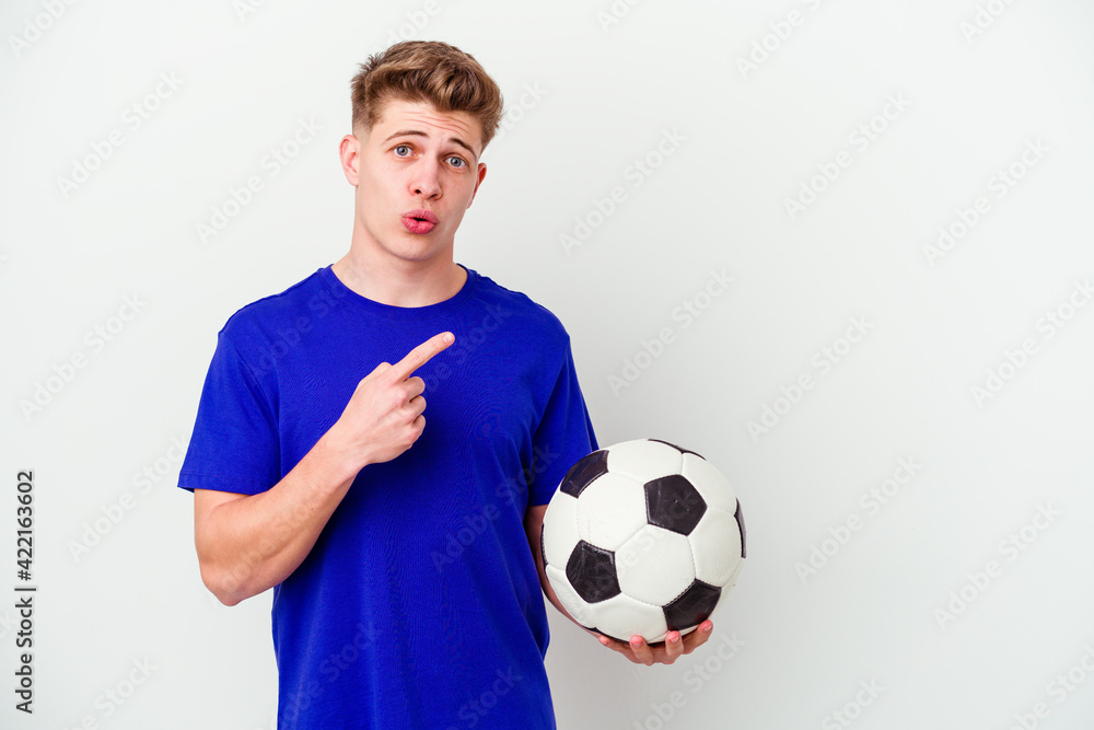 Young caucasian man playing soccer isolated on background pointing to the side