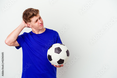 Young caucasian man playing soccer isolated on background touching back of head, thinking and making a choice.