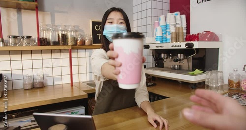 POV Happy female barista giving beverage cup to customer and smiling. Young Asian waitrees in medical mask hodling out order and saying goodbye . Hand taking drink. Service, quarantine concept. photo