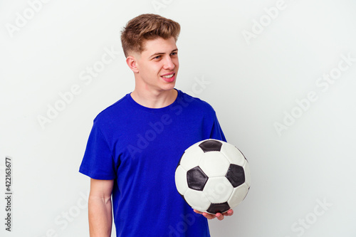 Young caucasian man playing soccer isolated on background looks aside smiling, cheerful and pleasant.