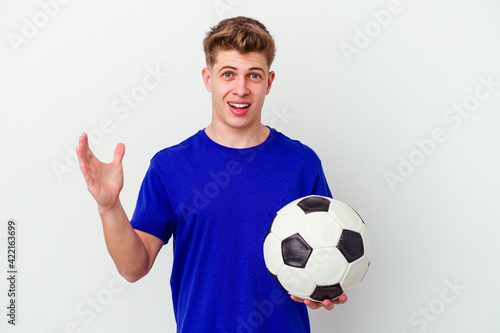 Young caucasian man playing soccer isolated on background receiving a pleasant surprise, excited and raising hands.