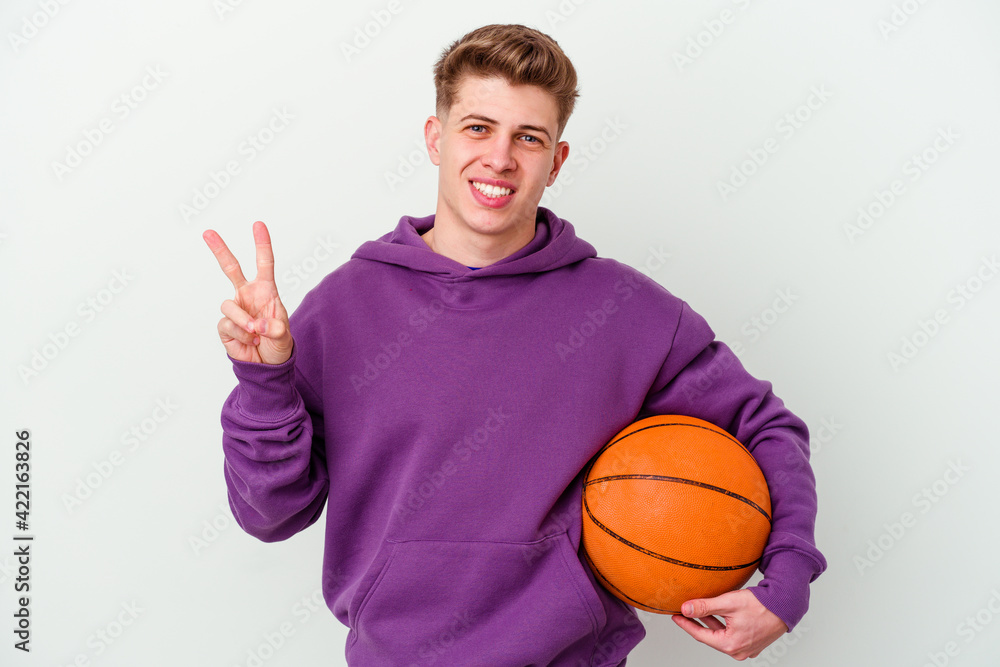Young caucasian man playing basketball isolated background joyful and carefree showing a peace symbol with fingers.