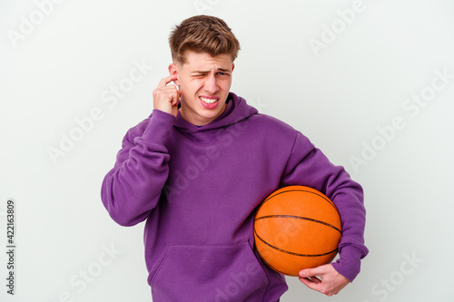 Young caucasian man playing basketball isolated background covering ears with hands.