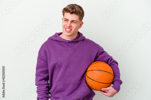 Young caucasian man playing basketball isolated background looks aside smiling, cheerful and pleasant.