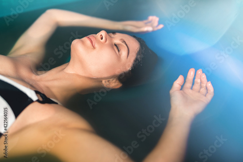 Beautiful woman floating in tank filled with dense salt water used in meditation, therapy, and alternative medicine. photo
