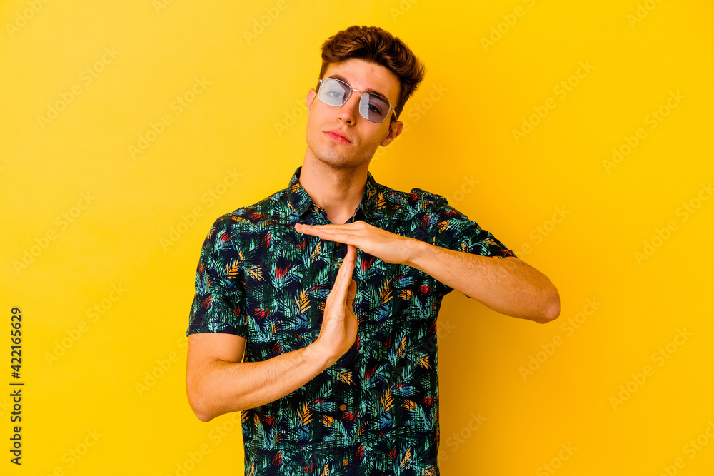 Young caucasian man wearing a Hawaiian shirt isolated on yellow background showing a timeout gesture. - obrazy, fototapety, plakaty 