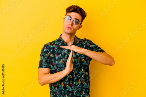 Young caucasian man wearing a Hawaiian shirt isolated on yellow background showing a timeout gesture.