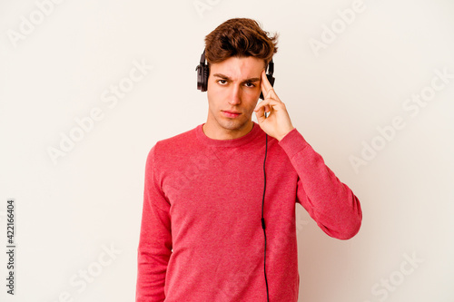 Young caucasian man listening to music isolated on white background pointing temple with finger, thinking, focused on a task.