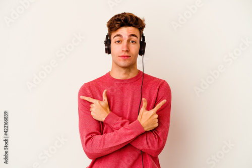 Photography Young caucasian man listening to music isolated on white background points sideways, is trying to choose between two options