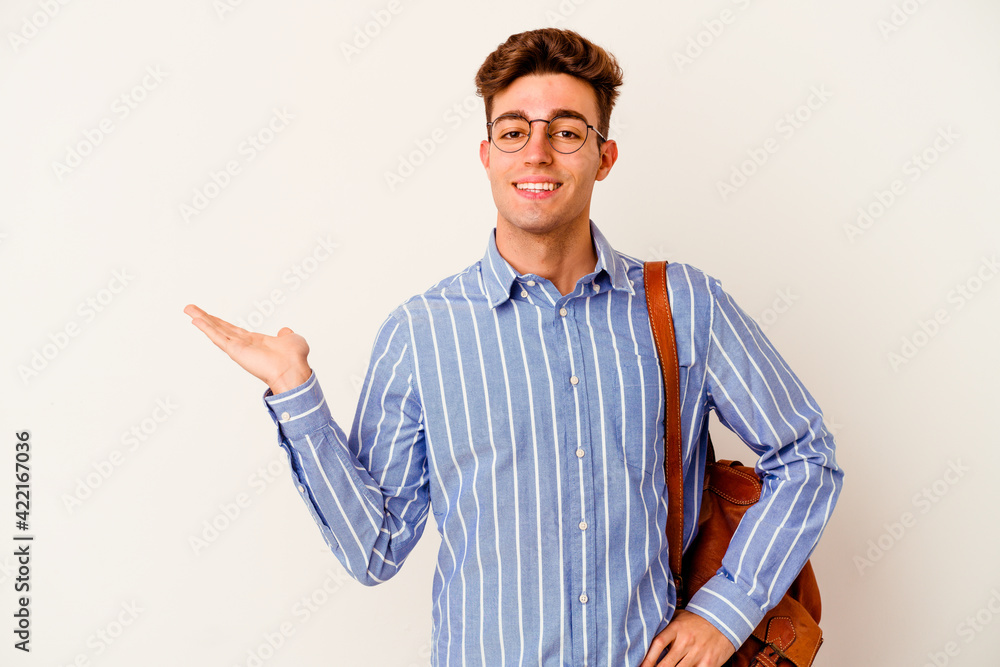 Young student man isolated on white background showing a copy space on a palm and holding another hand on waist. Young student man isolated on white background showing a copy space on a palm and holding another hand on waist.