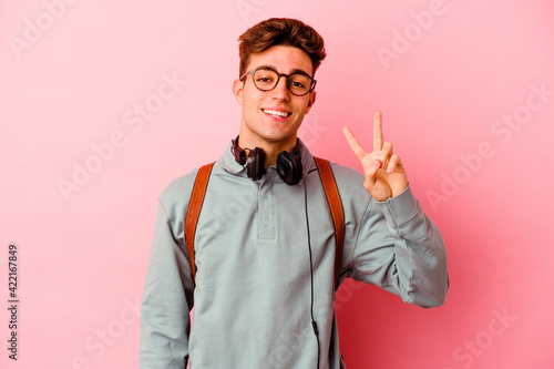 Young student man isolated on pink background showing victory sign and smiling broadly.