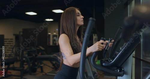 Young attractive athletic sports woman with handsome buttocks doing exercises at elipsoid machine in gym. Slow motion photo