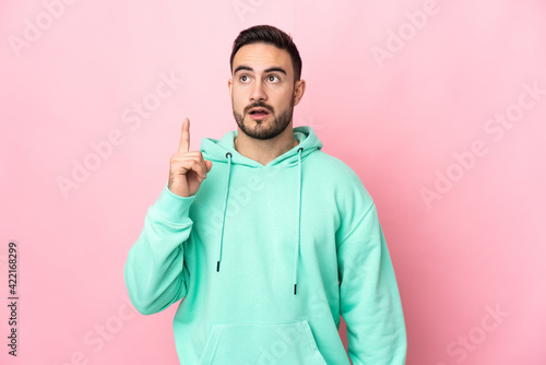 Young caucasian handsome man isolated on pink background thinking an idea pointing the finger up © luismolinero