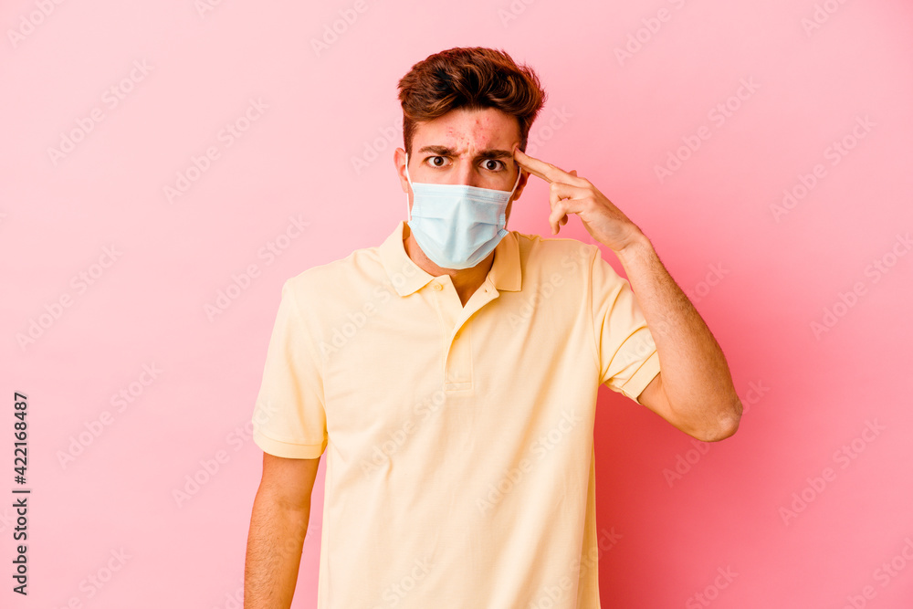 Young caucasian man wearing a protection for coronavirus isolated on pink background showing a disappointment gesture with forefinger.