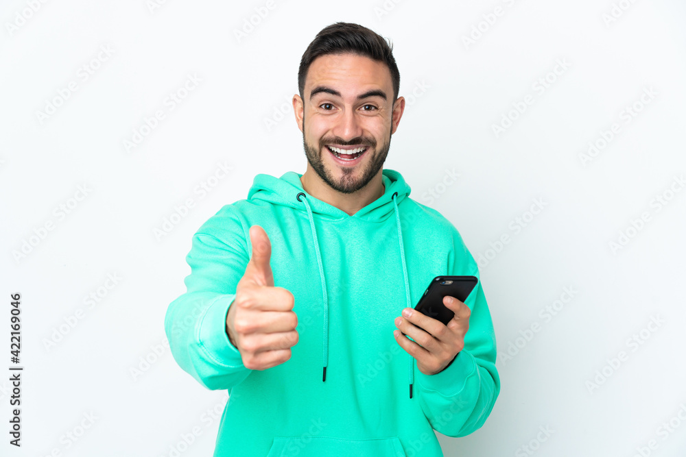 Young caucasian handsome man isolated on white background using mobile phone while doing thumbs up Young caucasian handsome man isolated on white background using mobile phone while doing thumbs up