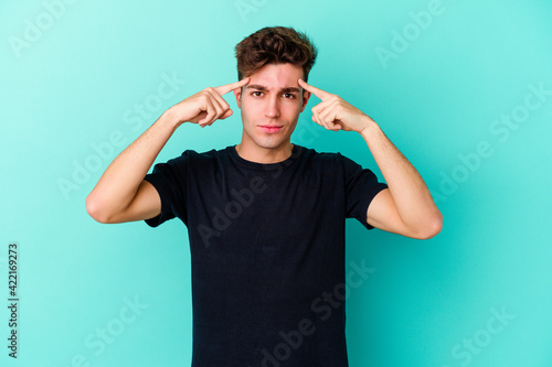Obraz na płótnie Young caucasian man isolated on blue background focused on a task, keeping forefingers pointing head