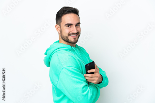 Young caucasian handsome man isolated on white background holding a mobile phone and with arms crossed
