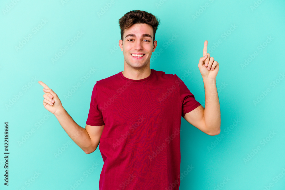 Young caucasian man isolated on blue background pointing to different copy spaces, choosing one of them, showing with finger. Young caucasian man isolated on blue background pointing to different copy spaces, choosing one of them, showing with finger.