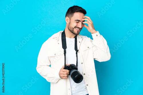 Young photographer man isolated on blue background laughing