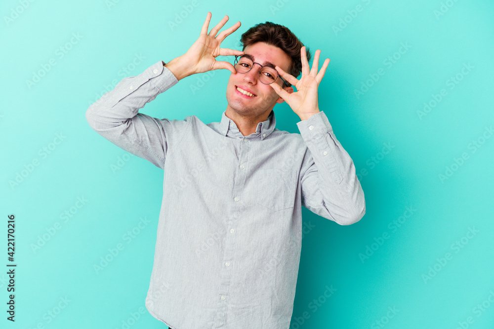 Young caucasian man isolated on blue background showing okay sign over eyes Young caucasian man isolated on blue background showing okay sign over eyes