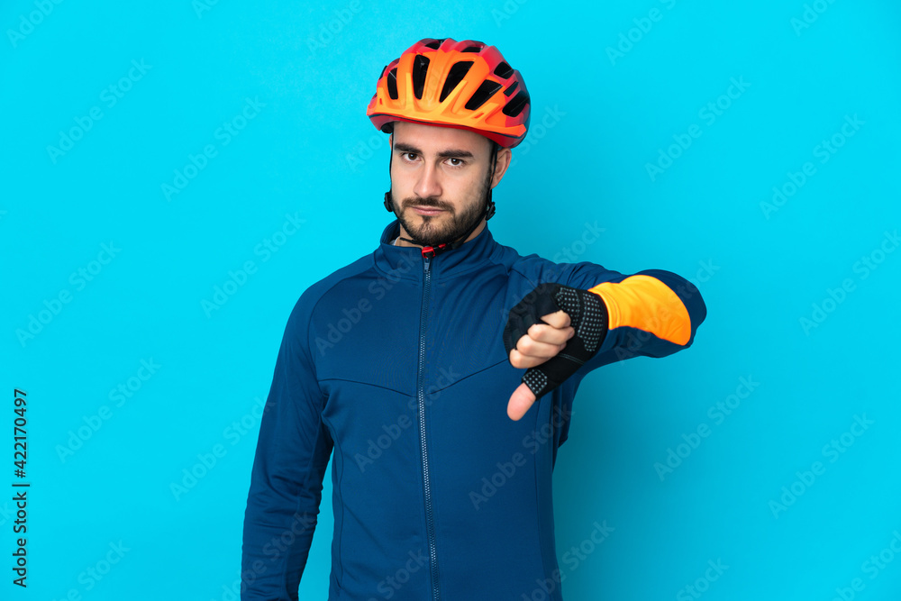 Young cyclist man isolated on blue background showing thumb down with negative expression