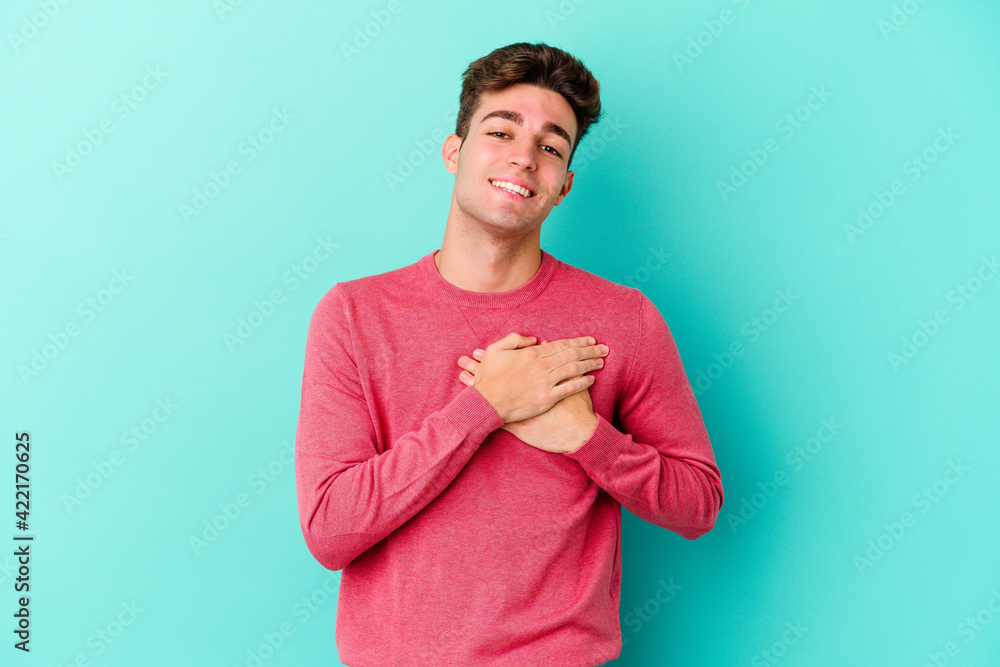 Young caucasian man isolated on blue background has friendly expression, pressing palm to chest. Love concept. Young caucasian man isolated on blue background has friendly expression, pressing palm to chest. Love concept.