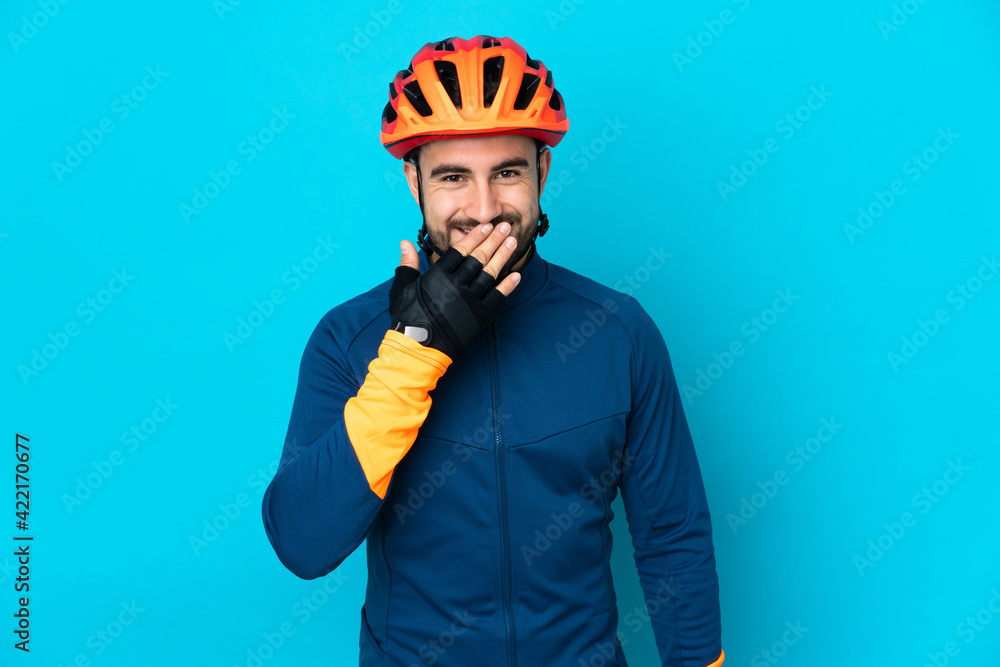 Young cyclist man isolated on blue background happy and smiling covering mouth with hand Young cyclist man isolated on blue background happy and smiling covering mouth with hand