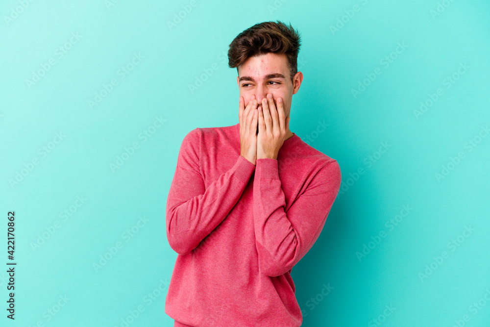 Young caucasian man isolated on blue background laughing about something, covering mouth with hands. Young caucasian man isolated on blue background laughing about something, covering mouth with hands.