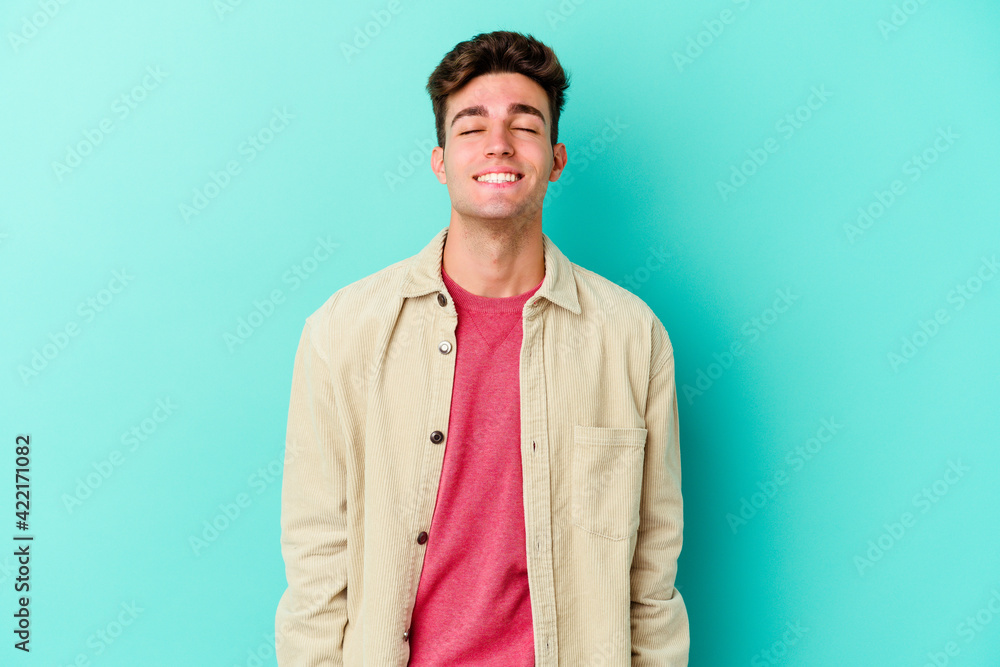 Young caucasian man isolated on blue background laughs and closes eyes, feels relaxed and happy. Young caucasian man isolated on blue background laughs and closes eyes, feels relaxed and happy.