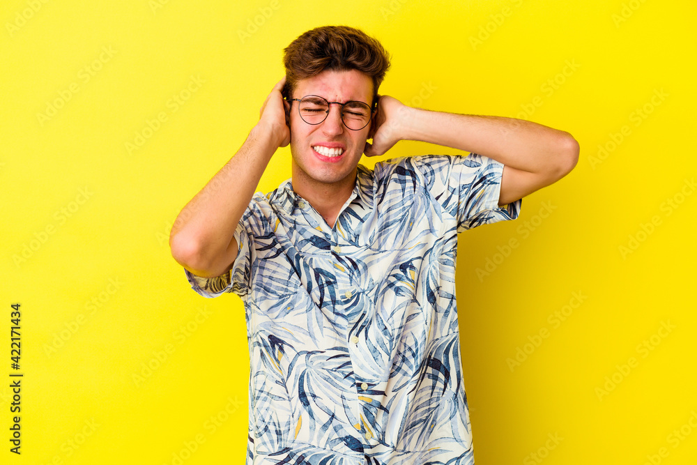 Young caucasian man isolated on yellow background covering ears with hands. Young caucasian man isolated on yellow background covering ears with hands.