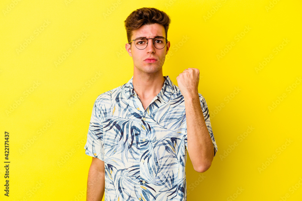 Young caucasian man isolated on yellow background showing fist to camera, aggressive facial expression. Young caucasian man isolated on yellow background showing fist to camera, aggressive facial expression.