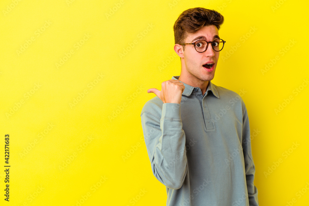 Young caucasian man isolated on yellow background points with thumb finger away, laughing and carefree. Young caucasian man isolated on yellow background points with thumb finger away, laughing and carefree.