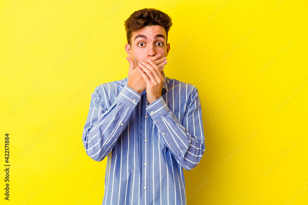 Young caucasian man isolated on yellow background shocked covering mouth with hands. Young caucasian man isolated on yellow background shocked covering mouth with hands.