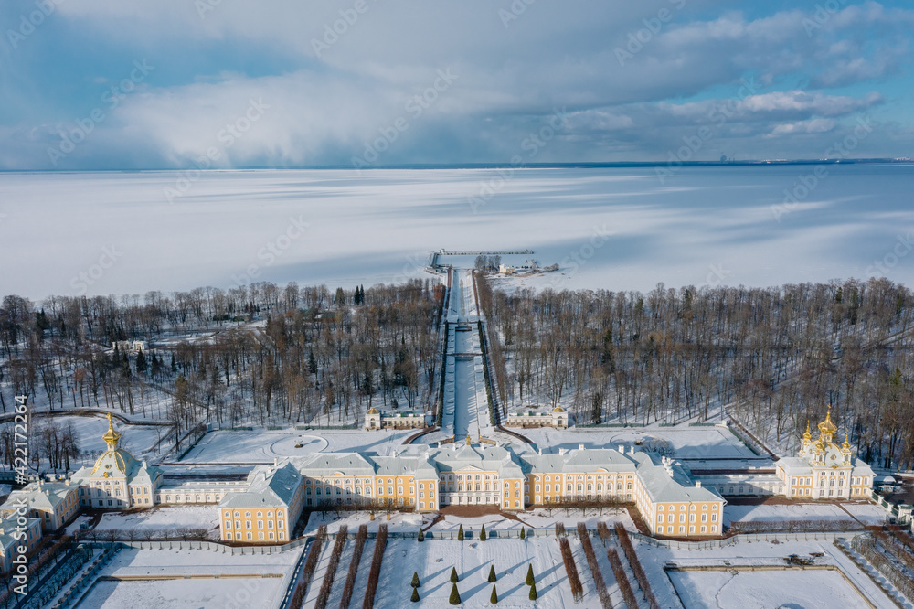 Panoramic aerial view of the Grand Palace and the park with fountains in winter in Peterhof. The upper garden is closed for restoration, blue sky, sunny day, white snow. Russia, Peterhof, 02.21.2021 Panoramic aerial view of the Grand Palace and the park with fountains in winter in Peterhof. The upper garden is closed for restoration, blue sky, sunny day, white snow. Russia, Peterhof, 02.21.2021