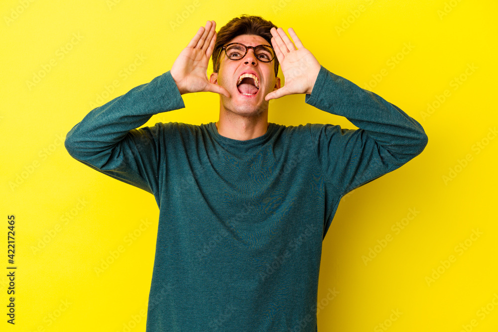 Young caucasian man isolated on yellow background shouting excited to front. Young caucasian man isolated on yellow background shouting excited to front.